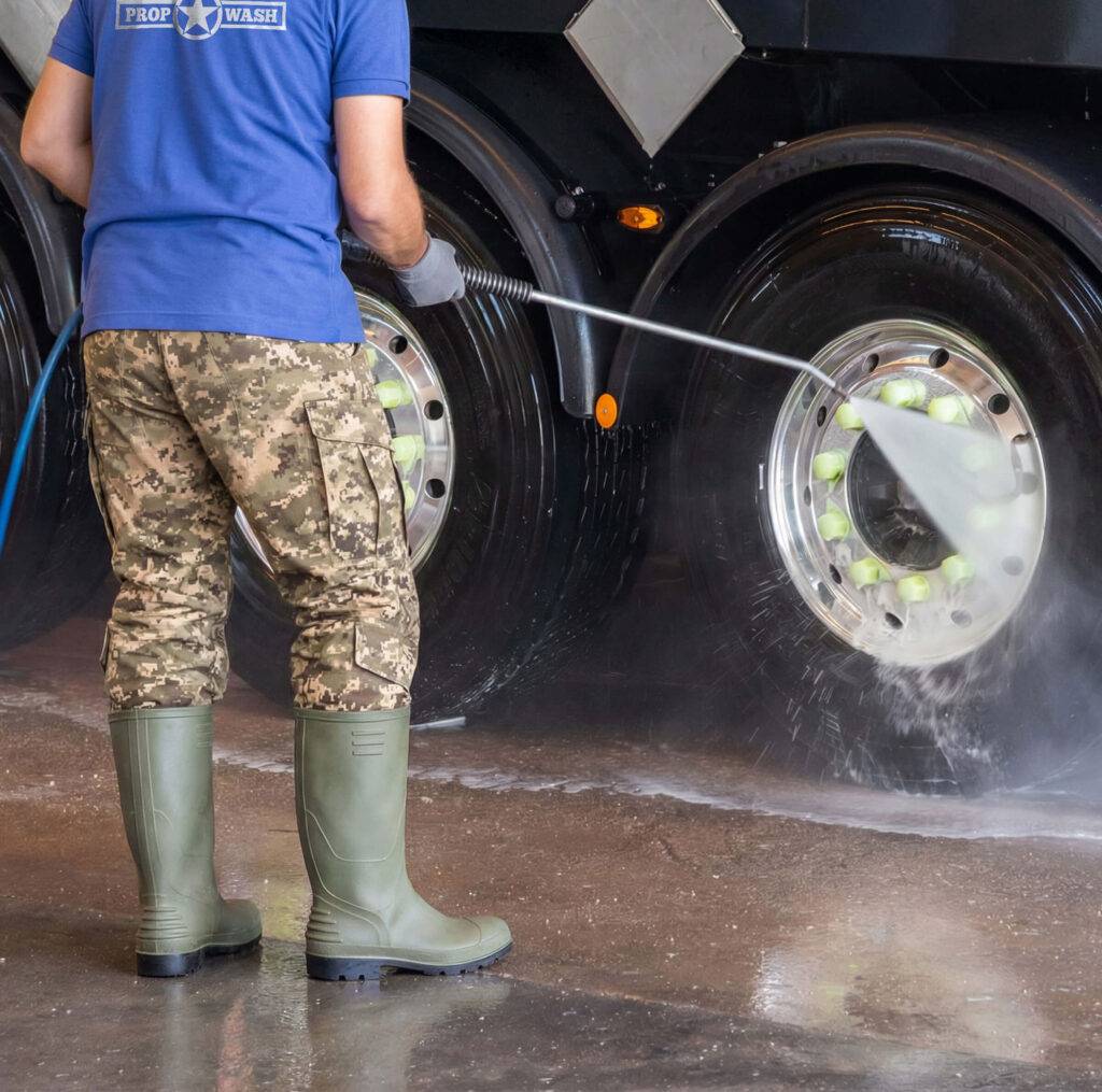 man spraying dirt off of large truck tires