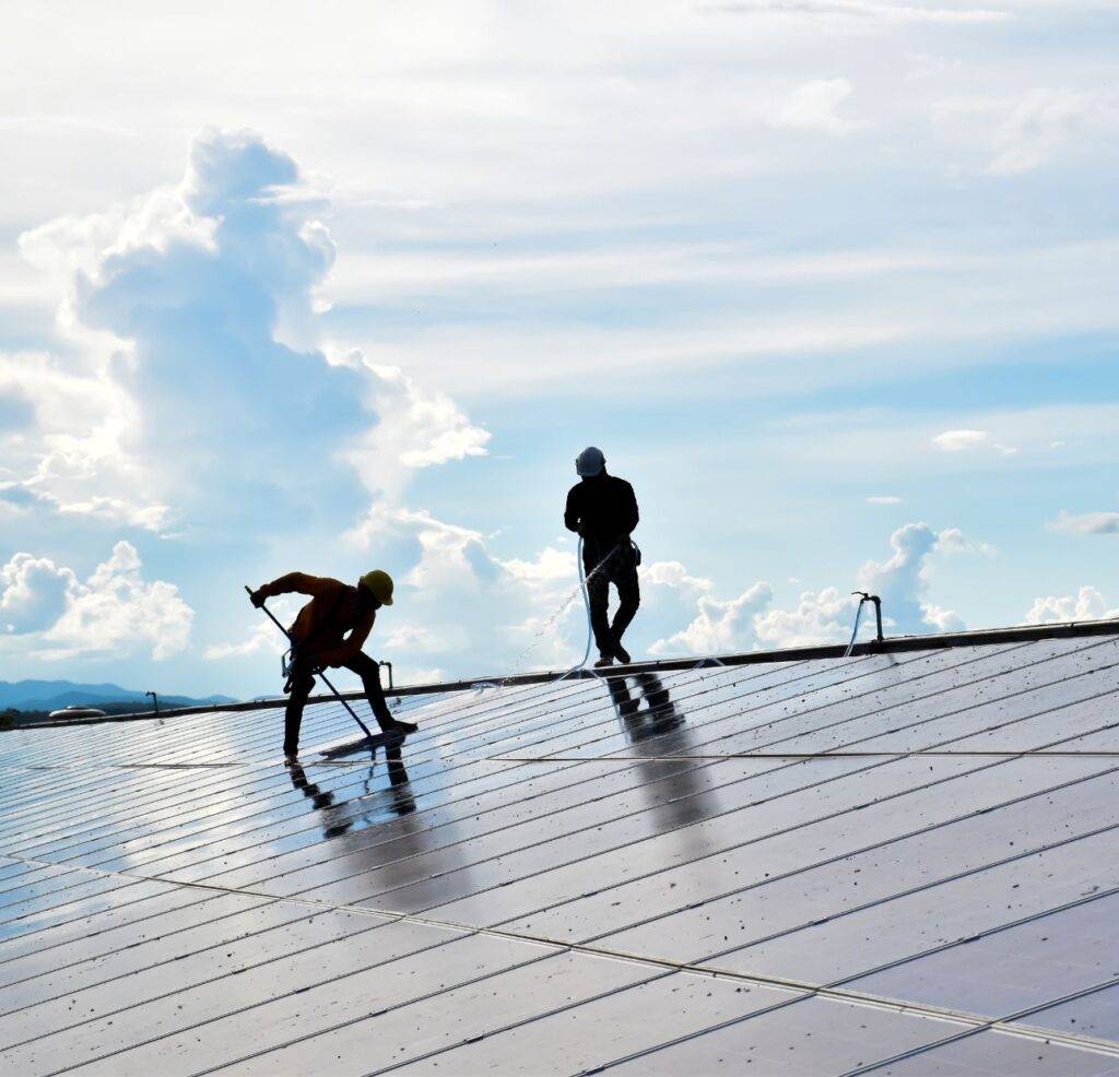 two prop wash employees on roof power washing solar panels