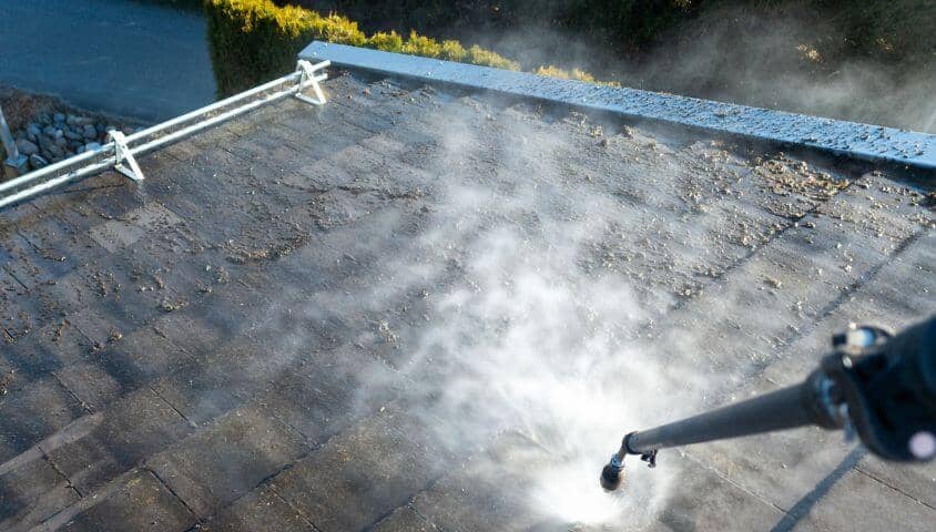 A pressure washer hose spraying a dirty roof